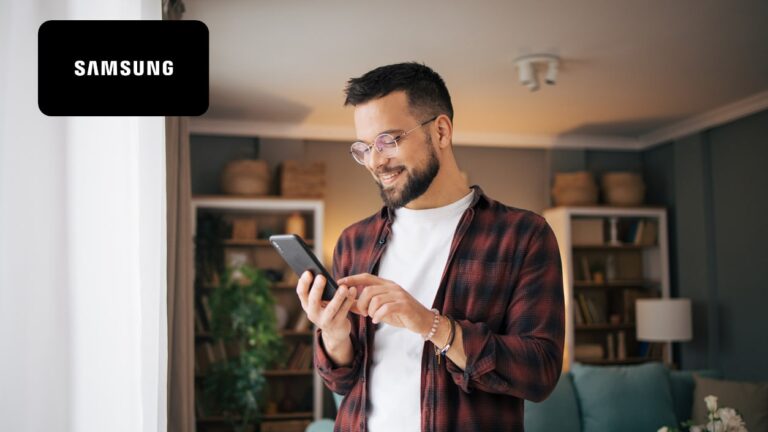 An adult man is standing in a modern living room by the window and using a smartphone to talk.