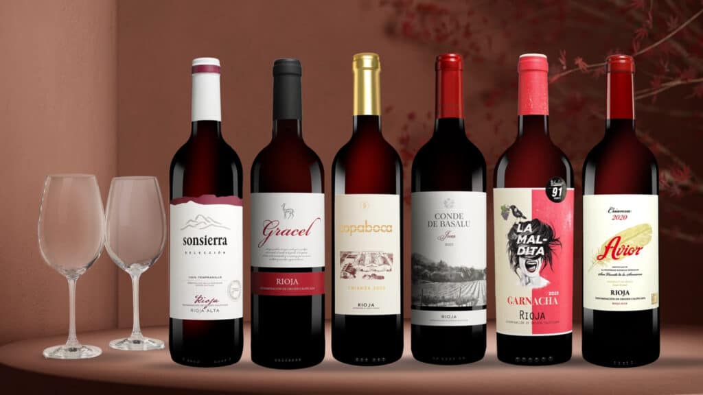 Sechs Flaschen Rioja-Rotwein stehen auf einem Tisch. Daneben stehen zwei Wein-Gläser.