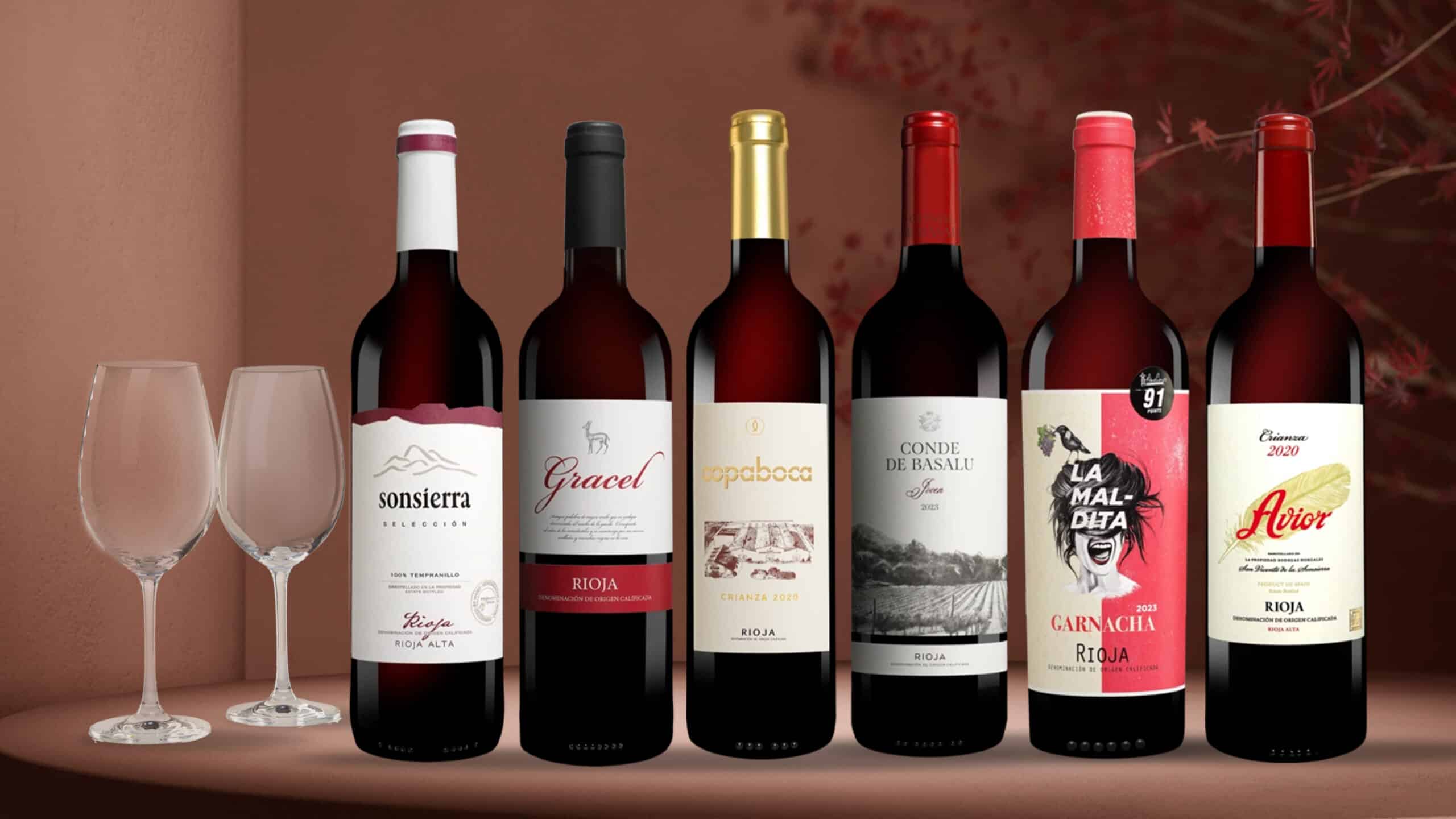 Sechs Flaschen Rioja-Rotwein stehen auf einem Tisch. Daneben stehen zwei Wein-Gläser.