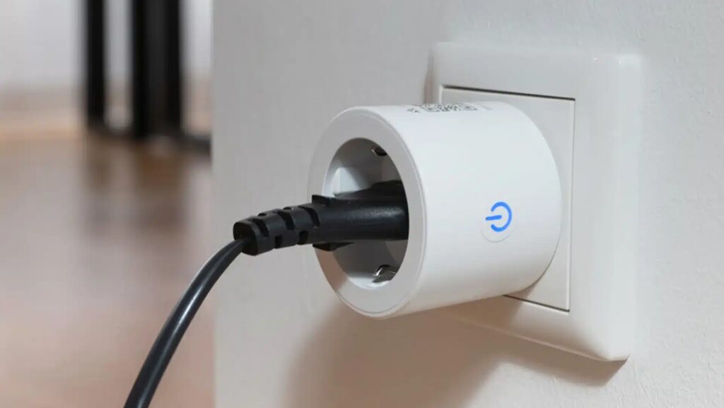Weiße Steckdose in der ein runder weißer Stecker steckt in dem ein schwarzer Gerätestecker mit Kabel steckt an weißer Wandecke