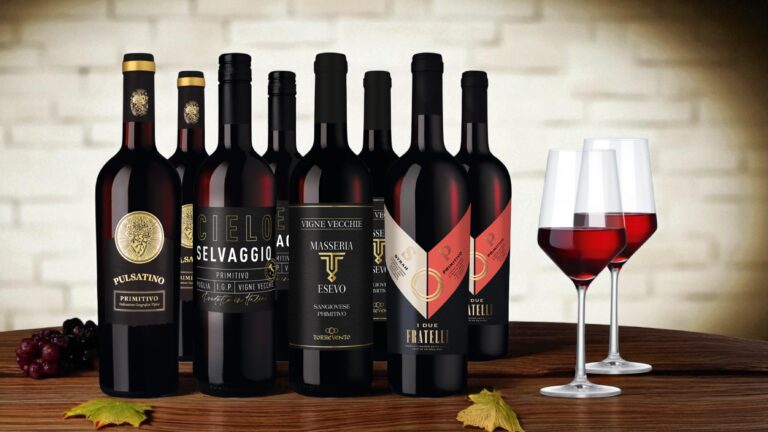 Acht Flaschen Rotwein mit zwei Gläsern auf einem Holztisch vor einer Steinwand