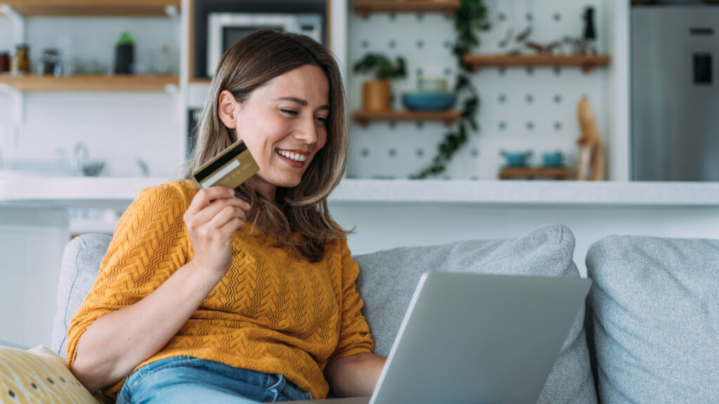Frau auf Couch mit Laptop und Kreditkarte