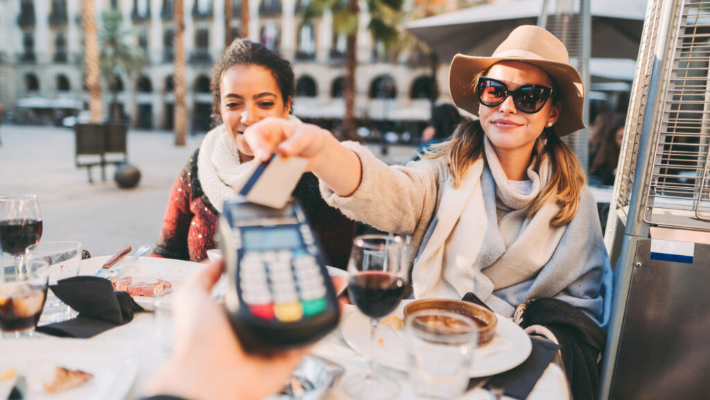 Frau mit Sonnenbrille bezahlt im Restaurant mit Kreditkarte.