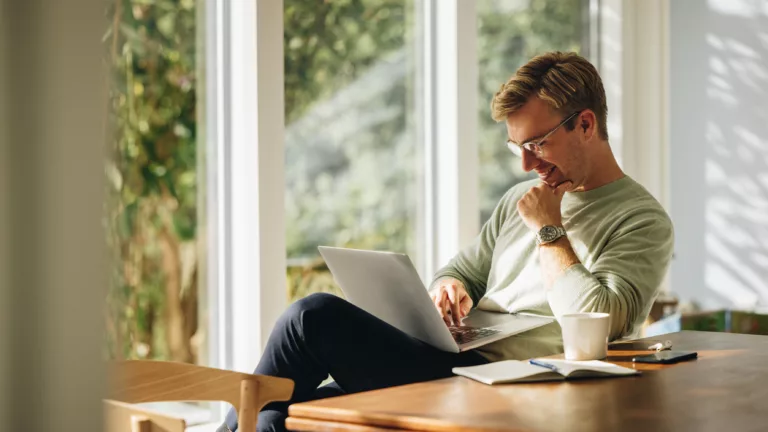 Junger Mann schaut lachend auf seinen Laptop in seinem Wohnzimmer. (@istockphoto.com)