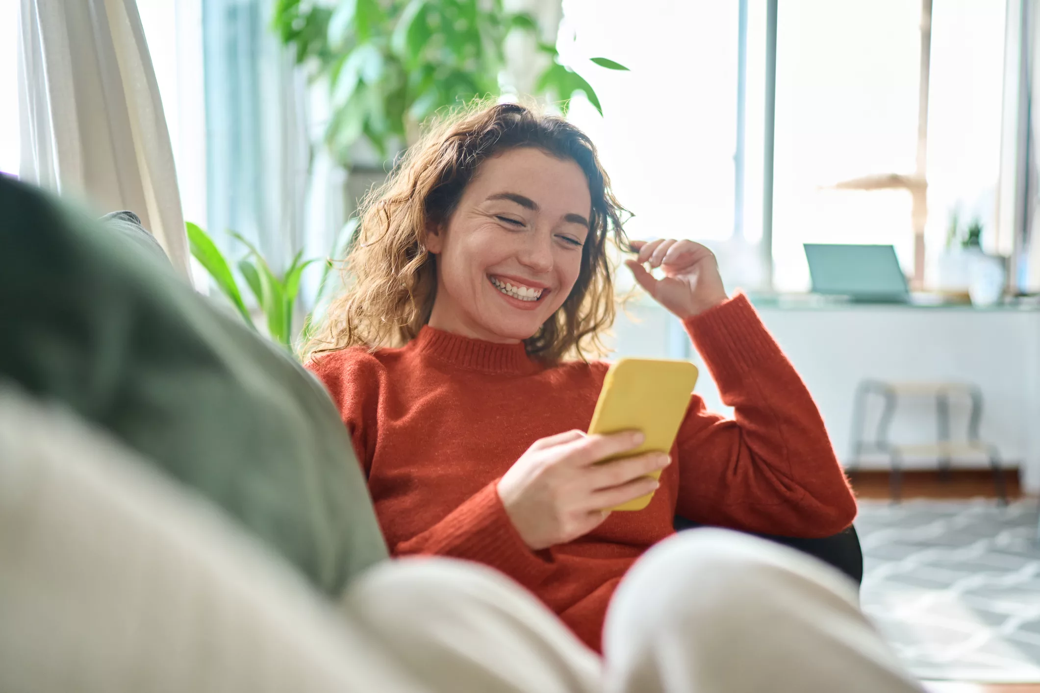 Happy relaxed young woman sitting on couch using mobile phone technology.