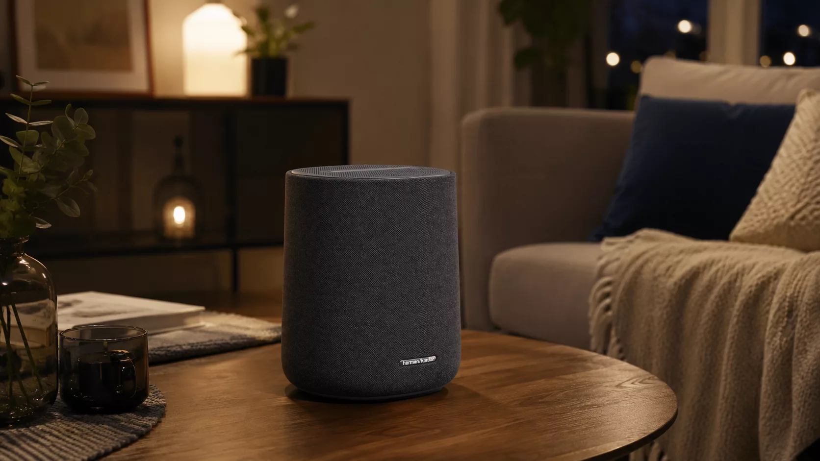 Der Harman-Kardon-Lautsprecher auf einem Holztisch in einem gemütlichen Wohnzimmer. (@KI-generiert / Harman Kardon)