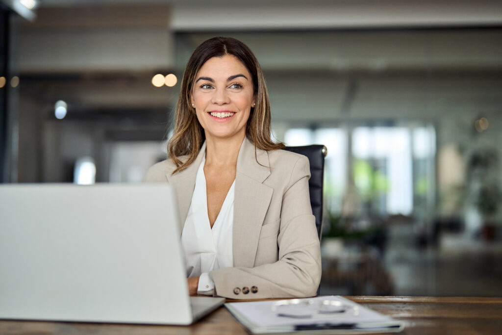 Glückliche, mittelalte Geschäftsfrau arbeitet im Büro am Laptop und blickt lächelnd in Richtung Copy Space. Reife Businessfrau, Führungskraft oder Anwältin am Arbeitsplatz, die über neue Ideen und Pläne nachdenkt. (@istockphoto)