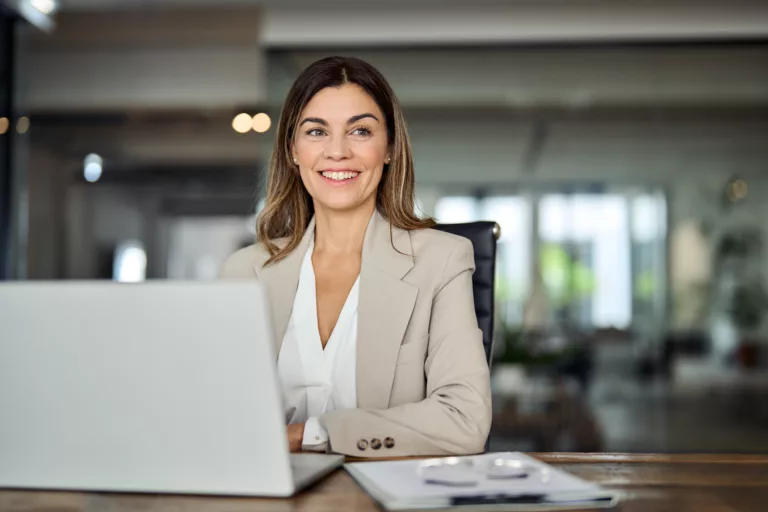 Glückliche, mittelalte Geschäftsfrau arbeitet im Büro am Laptop und blickt lächelnd in Richtung Copy Space. Reife Businessfrau, Führungskraft oder Anwältin am Arbeitsplatz, die über neue Ideen und Pläne nachdenkt. (@istockphoto)