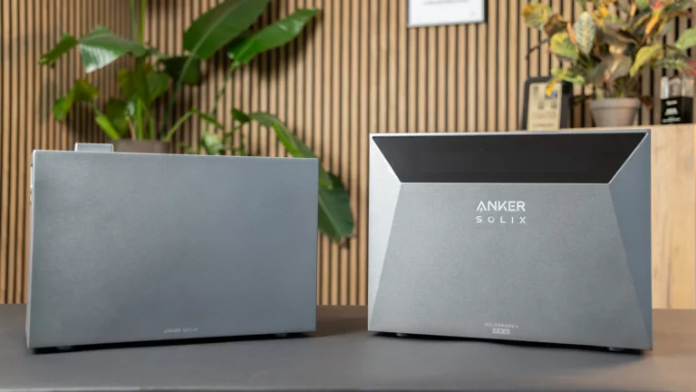 Die graue Anker Solix Solarbank 4 rechts mit Erweiterungsakku links vor braunem Holz mit grünen Pflanzen (@Anker)