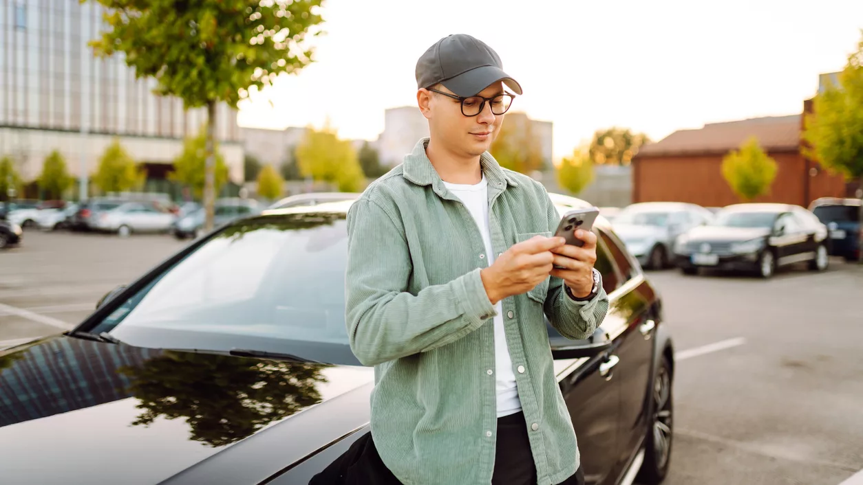Mann mit Handy vor Auto.