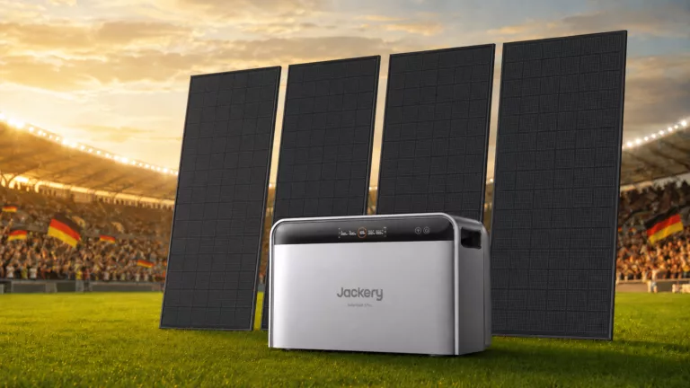 Ein Solarspeicher und vier Solarmodule stehen auf dem Rasen eines Fußballstadions, im Hintergrund sind deutschlandfahnen auf den Tribünen zu sehen.