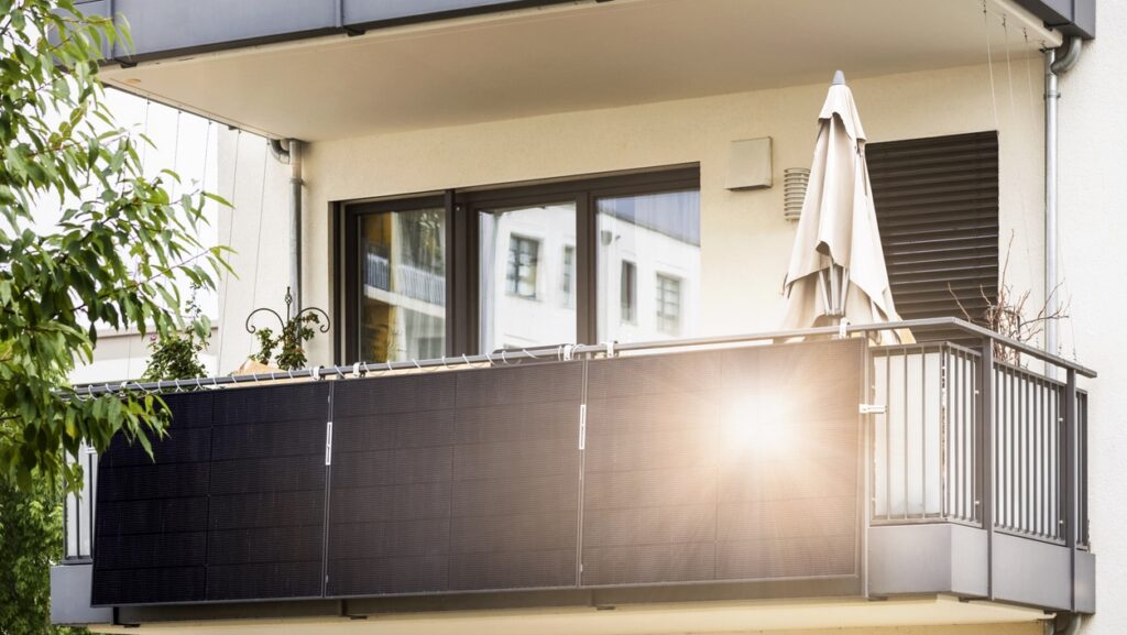 Balkon an modernem weißen Mehrfamilienhaus mit schwarzen Solarpanel am Geländer, die Sonne reflektieren