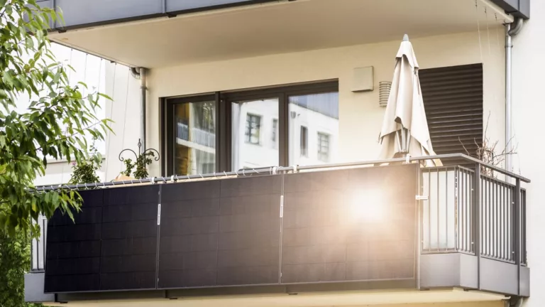Balkon an modernem weißen Mehrfamilienhaus mit schwarzen Solarpanel am Geländer, die Sonne reflektieren