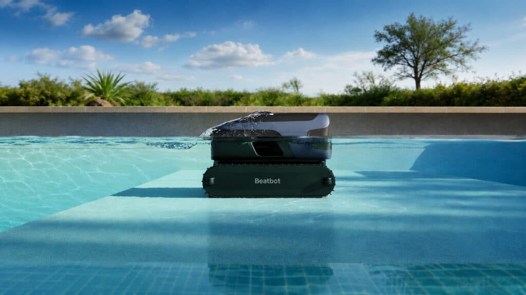 Querschnittsicht von einem Pool in dem ein dunkler Poolroboter von Beabto schwimmt, Pflanzen und blauer Himmel im Hintergrund