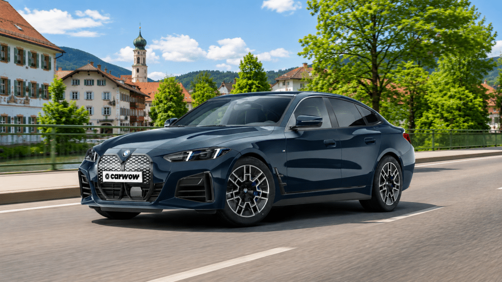 Dunkelblauer BMW i4 Coupé schräg von der Seite fährt auf Straße vor süddeutscher Stadtkulisse mit Bergen und Wald im Hintergrund bei blauem Himmel