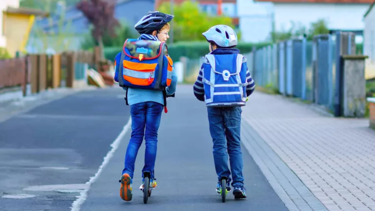 Zwei Jungen mit Schulranzen fahren City-Roller