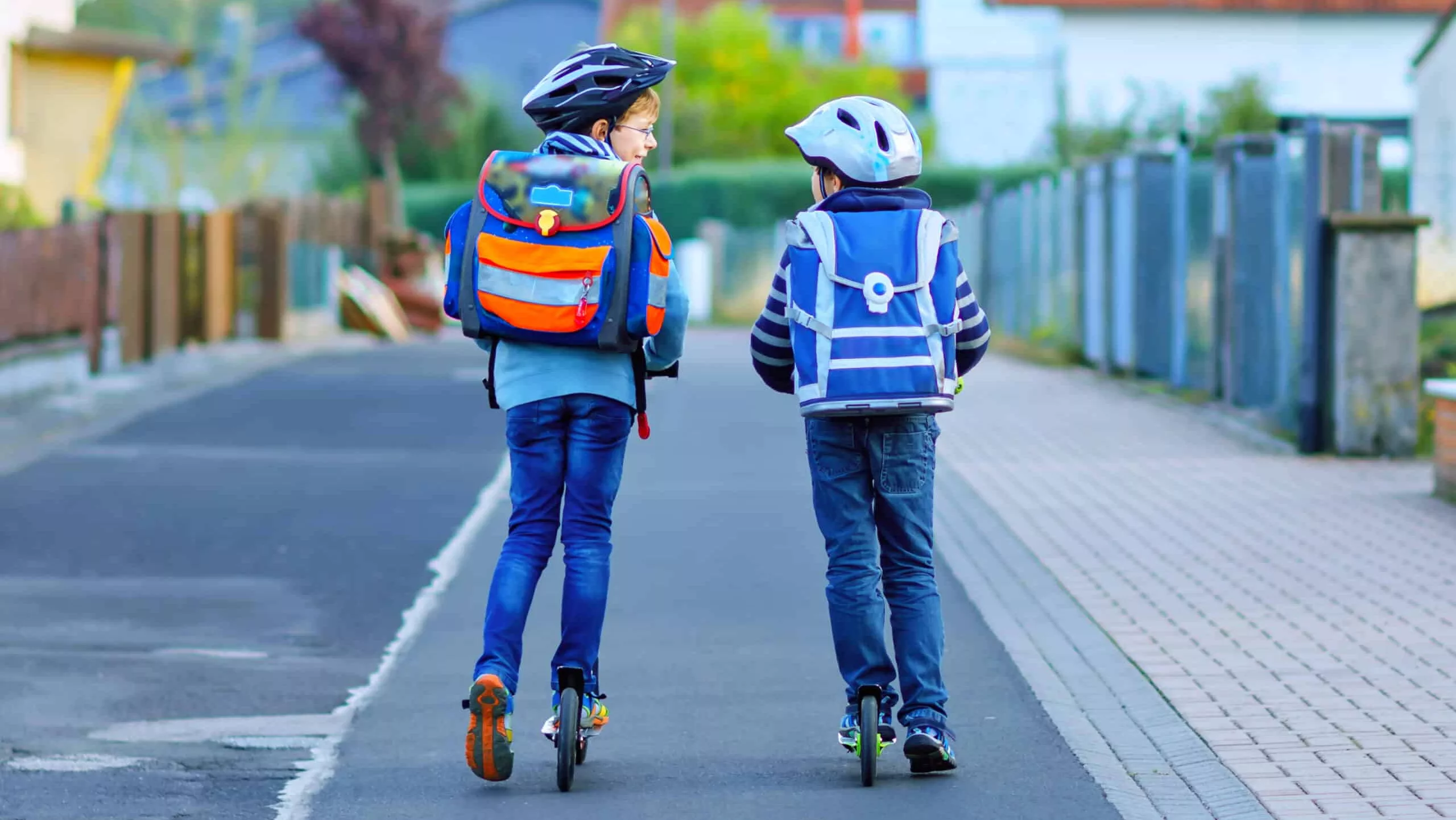 Zwei Jungen mit Schulranzen fahren City-Roller