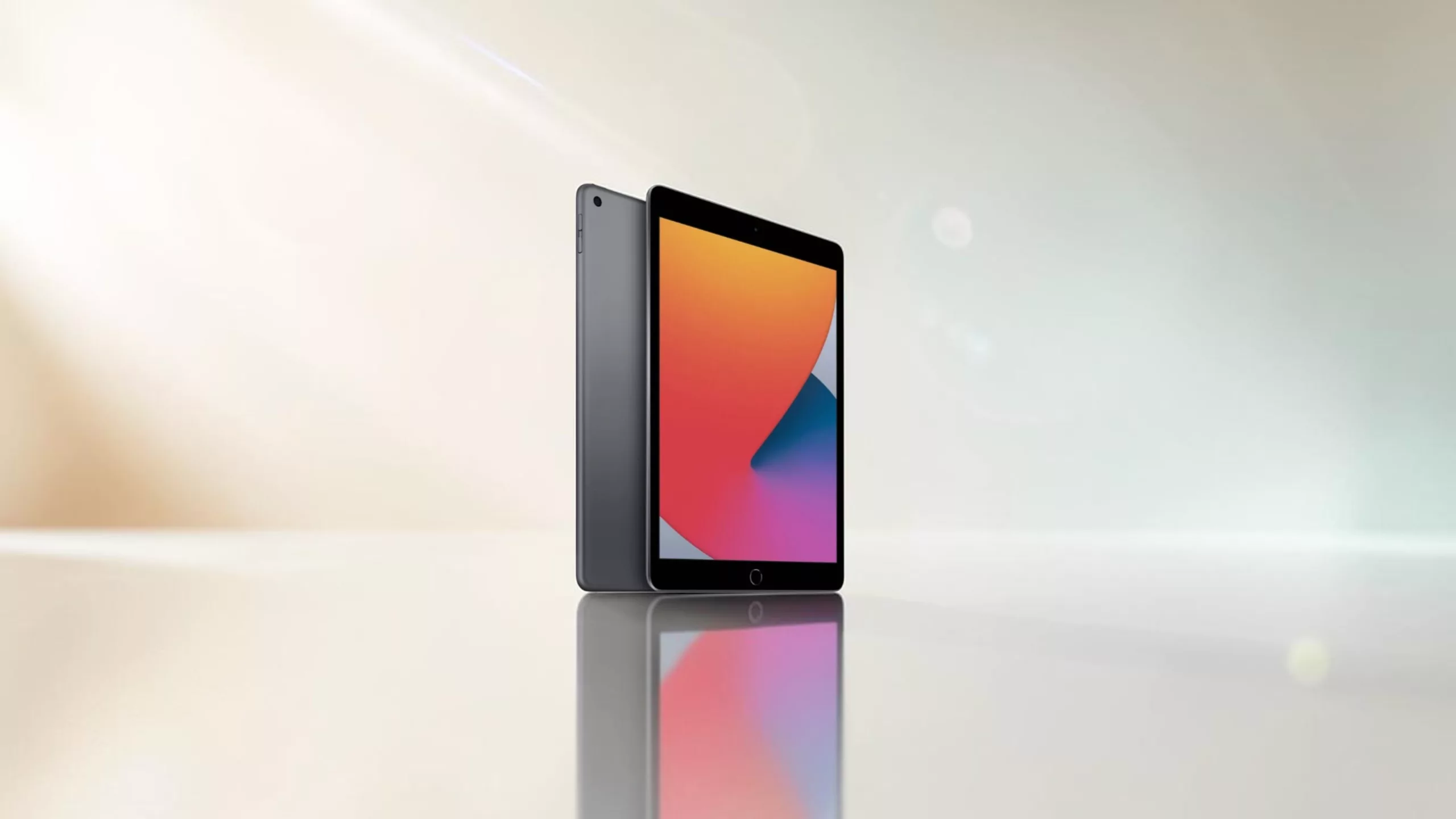 Graues Apple iPad Tablet schräg von der Seite von hinten und vorne mit bunten Farben auf Display auf einer spiegelnden Fläche gold blaugraue Farbverläufe und Lichtreflexionen im Hintergrund