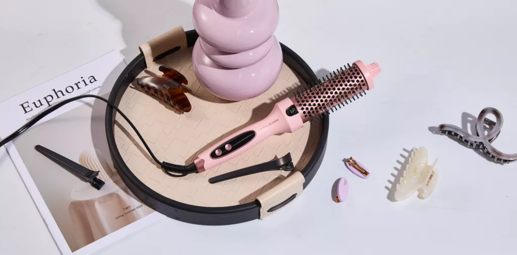 Wavytalk Thermobürste in Rosa liegt auf einem Tisch neben Haarspangen und einem Magazin