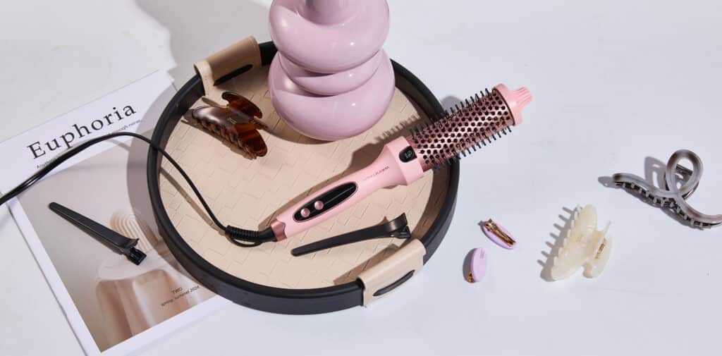 Wavytalk Thermobürste in Rosa liegt auf einem Tisch neben Haarspangen und einem Magazin