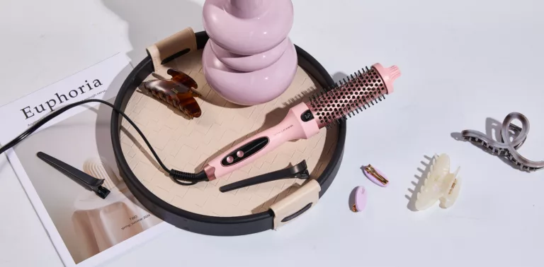 Wavytalk Thermobürste in Rosa liegt auf einem Tisch neben Haarspangen und einem Magazin