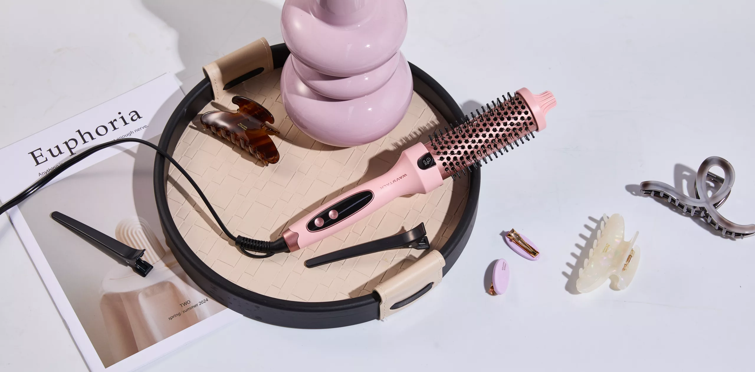 Wavytalk Thermobürste in Rosa liegt auf einem Tisch neben Haarspangen und einem Magazin