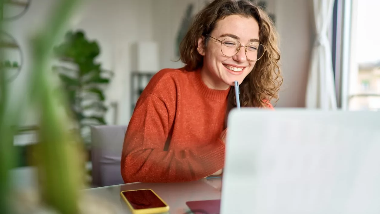 Junge glückliche Studentin mit Laptop und Webinar-Schreiben zu Hause