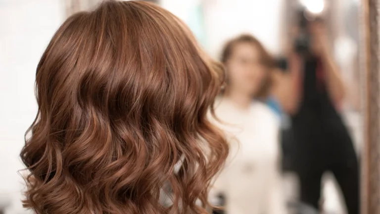 Wunderschönes Styling von welligem Haar bei einer jungen Frau mit mittelbraunen Haaren in einem Innenraum, Ansicht von hinten mit Spiegelbild, Nahaufnahme