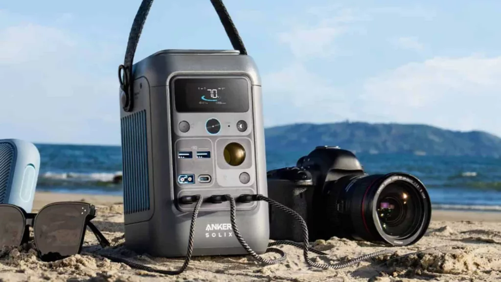 Graue Anker Solix Powerstation am Strand mit Nikon Kamera daneben vor blauem Himmel