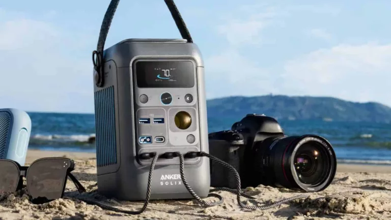 Graue Anker Solix Powerstation am Strand mit Nikon Kamera daneben vor blauem Himmel