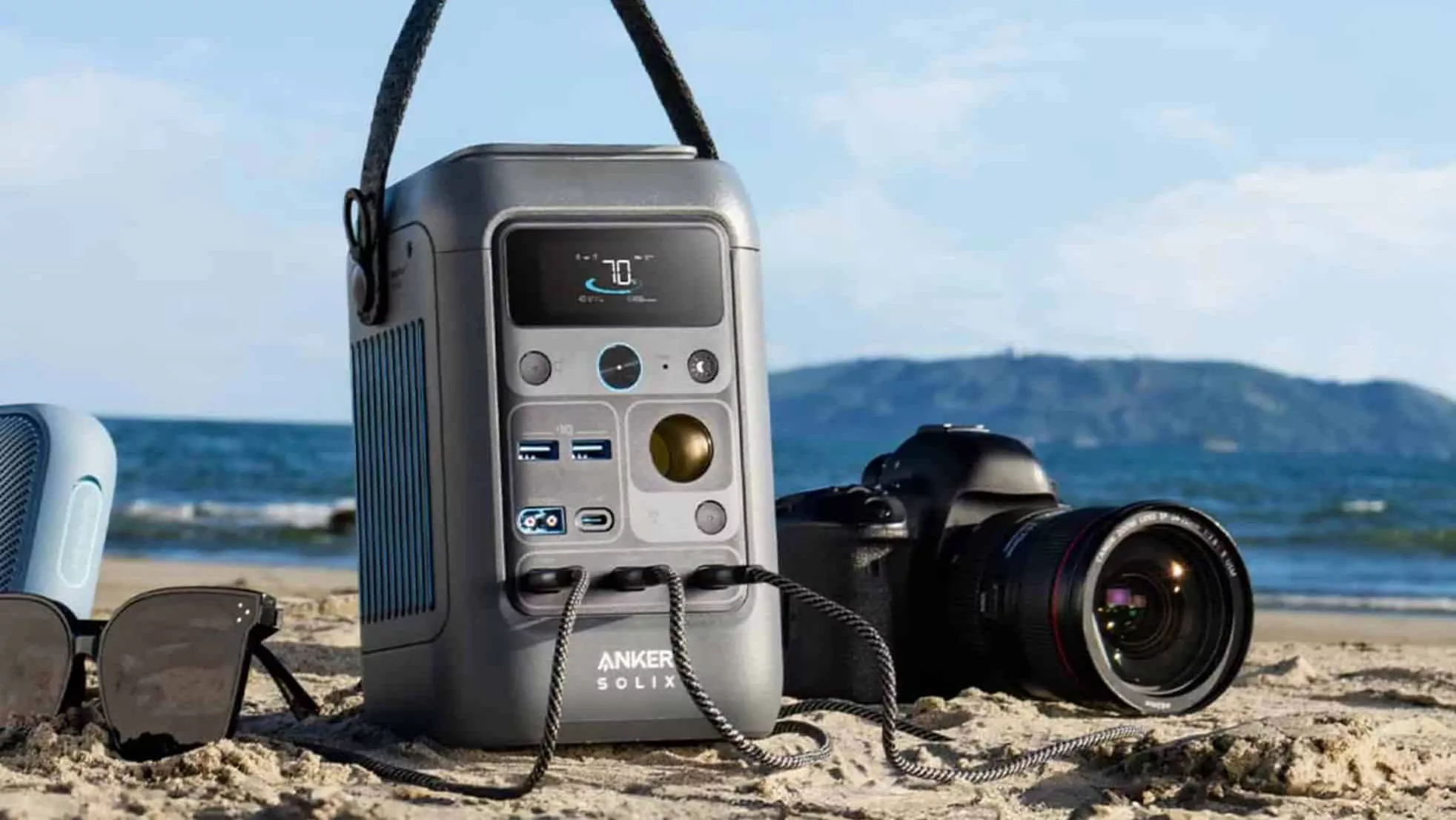 Graue Anker Solix Powerstation am Strand mit Nikon Kamera daneben vor blauem Himmel