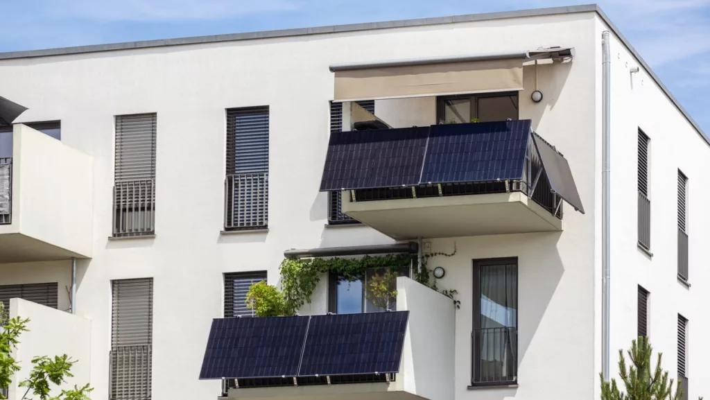 Weißes Mehrfamilienhaus mit zwei Balkonen mit je mehreren Solarmodulen an der Brüstung