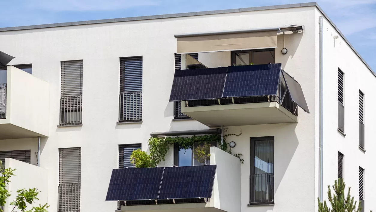 Weißes Mehrfamilienhaus mit zwei Balkonen mit je mehreren Solarmodulen an der Brüstung