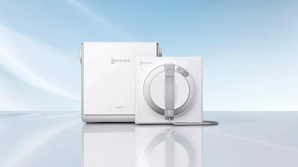 Weißer rechteckiger Ecovacs Fensterputzroboter von vorne mit weißer rechteckiger Station dahinter vor hellblau weißem Hintergrund auf spiegelnder Fläche
