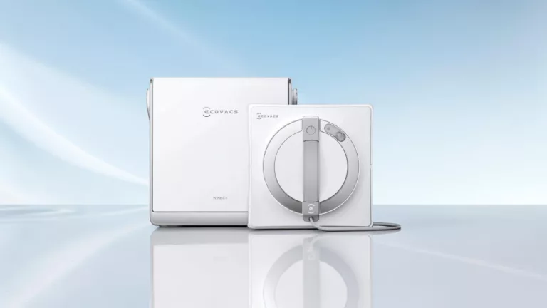 Weißer rechteckiger Ecovacs Fensterputzroboter von vorne mit weißer rechteckiger Station dahinter vor hellblau weißem Hintergrund auf spiegelnder Fläche