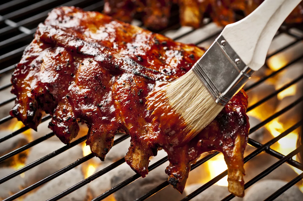 Rippchen wird mit Barbequesoße am Grill bepinselt