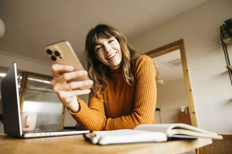 Frau, die zu Hause lächelnd ihr Smartphone und ihren Laptop benutzt