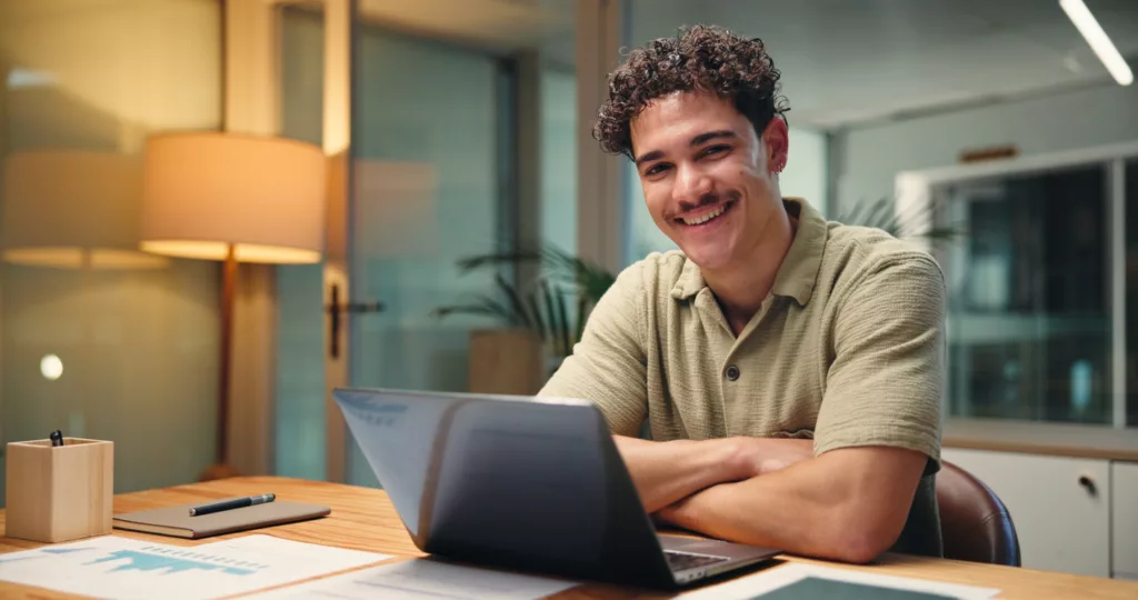 Mann am Laptop der glücklich in die Kamera schaut (@istock)