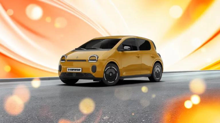 Oranger Renault Twingo E-Tech schräg von vorne auf grauem Straßenähnlichen Untergrund mit gelb orangenem Hintergrund und vielen runden Lichtreflexen vorne im Bild