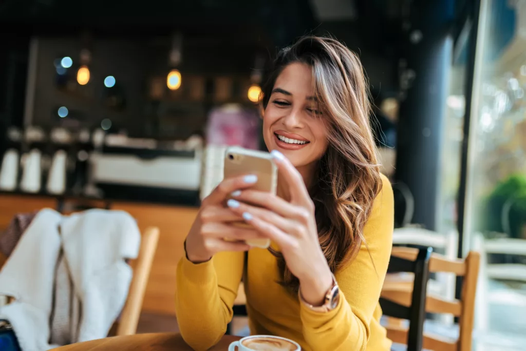 Glückliche Frau nutzt ihr Smartphone in einem Cafe (@istock)