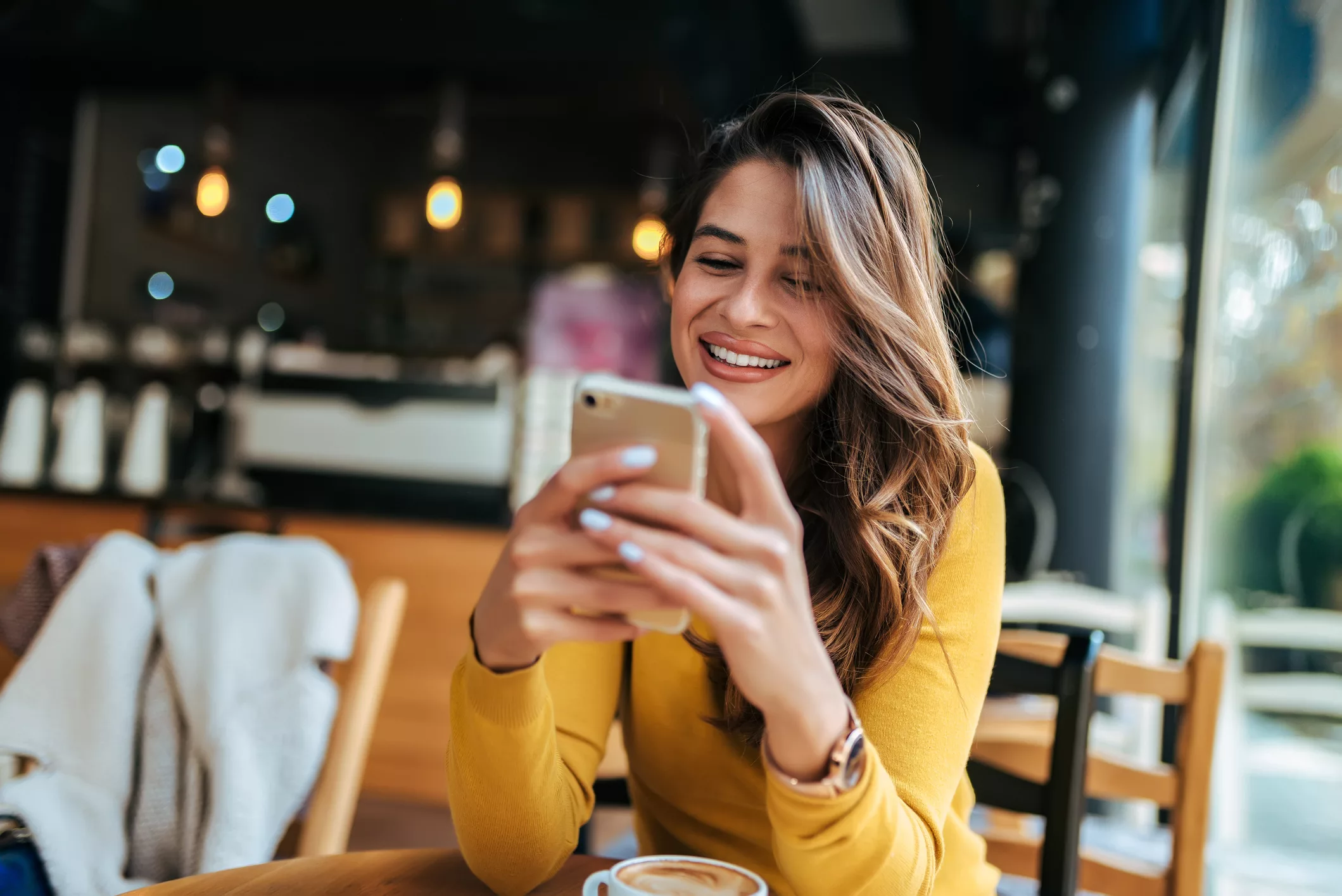 Glückliche Frau nutzt ihr Smartphone in einem Cafe (@istock)