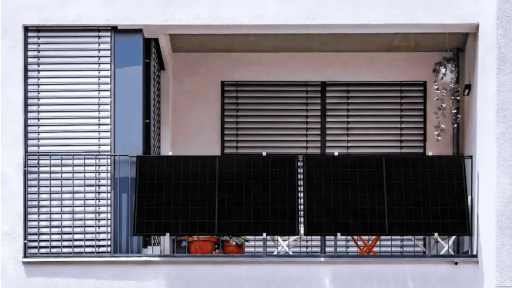 Balkon an weißer Hausfassade mit zwei schwarzen Solarpanels am Gitter