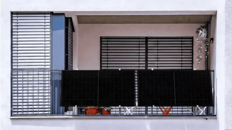 Balkon an weißer Hausfassade mit zwei schwarzen Solarpanels am Gitter