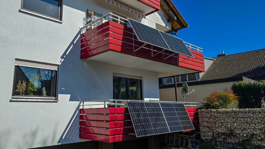 zwei rote Balkone an einem Mehrfamilienhaus, an beiden hängen Solarmodule