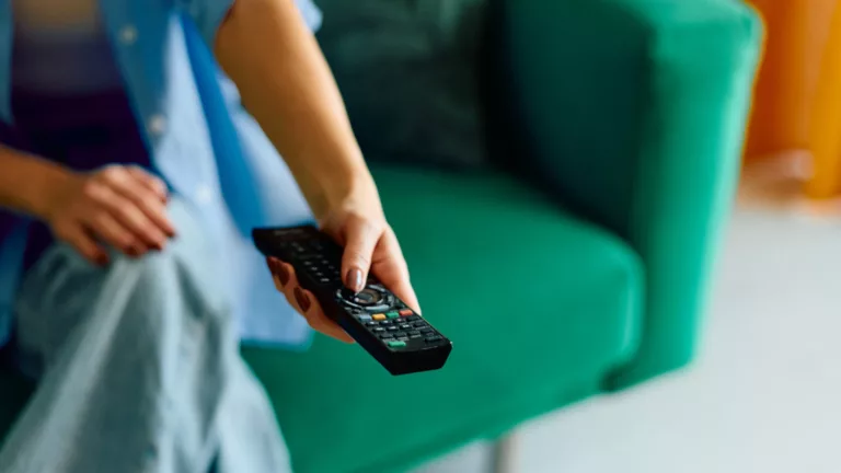 Frau auf einer grünen Couch mit Fernbedienung in der Hand