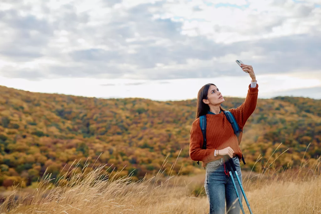 Eine Frau steht in der Wildnis und hängt ihr Telefon nach oben, um Netz zu bekommen. (@istock)