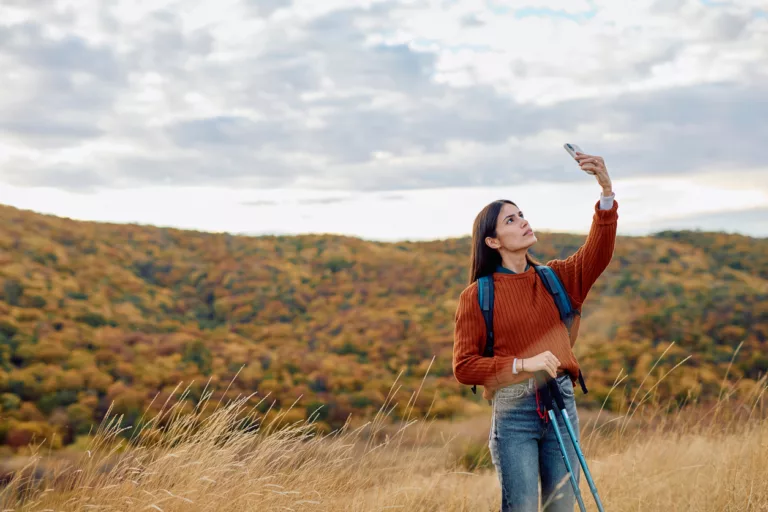 Eine Frau steht in der Wildnis und hängt ihr Telefon nach oben, um Netz zu bekommen. (@istock)