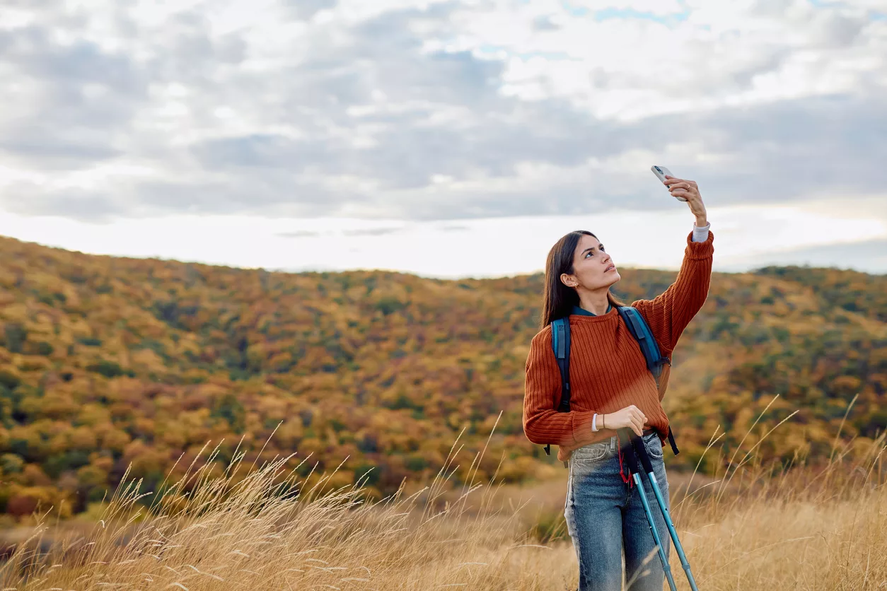 Eine Frau steht in der Wildnis und hängt ihr Telefon nach oben, um Netz zu bekommen. (@istock)
