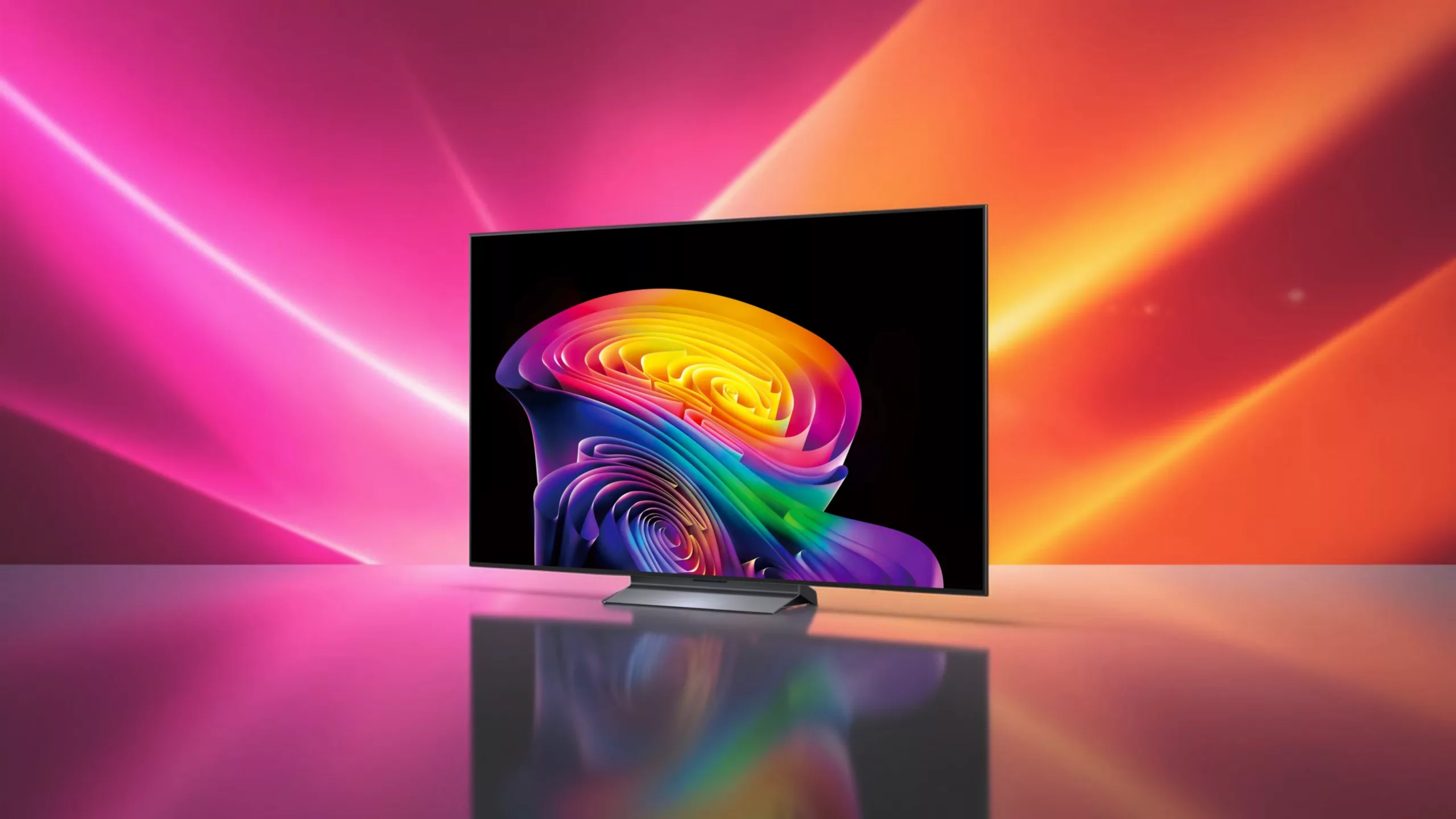 LG-Fernseher mit silbernem Standfuß schräg von vorne zeigt schwarzen Bildschirm mit einem bunten, knalligem Muster vor Pink orangenem Hintergrund mit Lichtstreifen auf spiegelnder Fläche