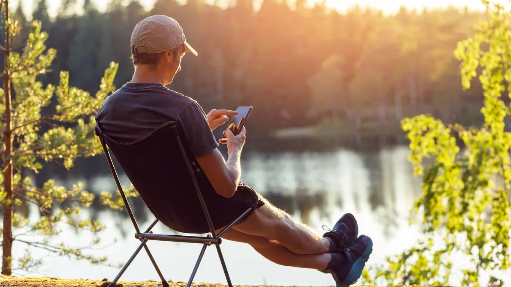 Mann mit Smartphone sitzt am Waldsee.